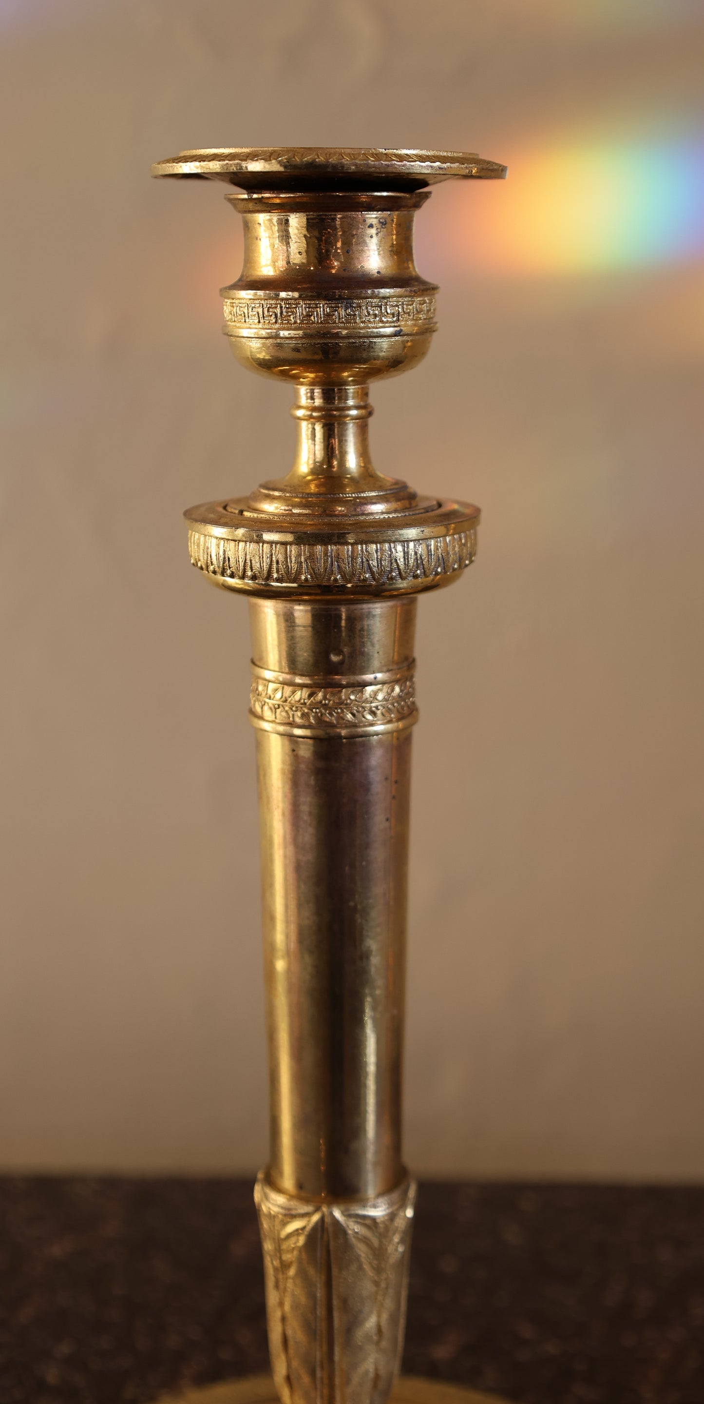 A close up picture of an empire candlestick from the 19th century. There is a rainbow ray in the background.