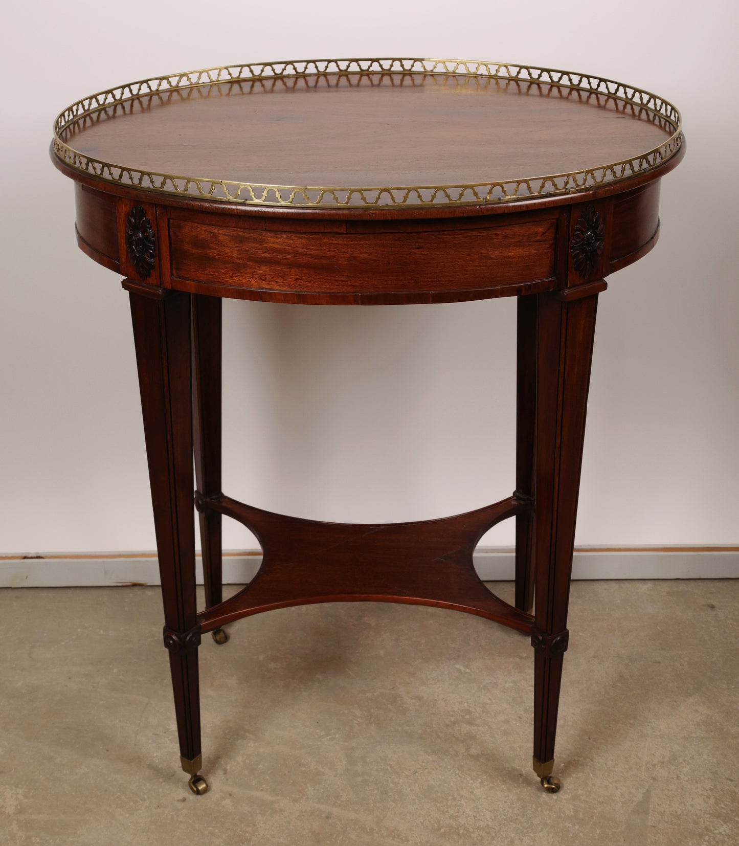 High-class Stockholm piece from around 1790. Crafted in veneered and partially solid mahogany with carved wooden decorations of corner florets. The core material is pine and alder. The top is fitted with a brass balustrade. The table features brass castors and includes a drawer in the apron with a key. Back view.