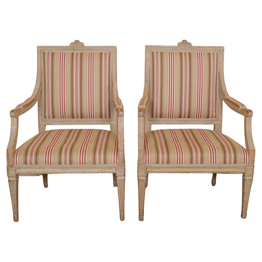 A pair of high Gustavian armchairs crafted in Sweden during the 1780s. These chairs feature a straight design with square legs. The top rail is adorned with a hop vine motif, with traces of the original paint still visible. Much of the original paint remains and has been carefully revealed. The leg joints to the rail are decorated with elegant florets. White background.