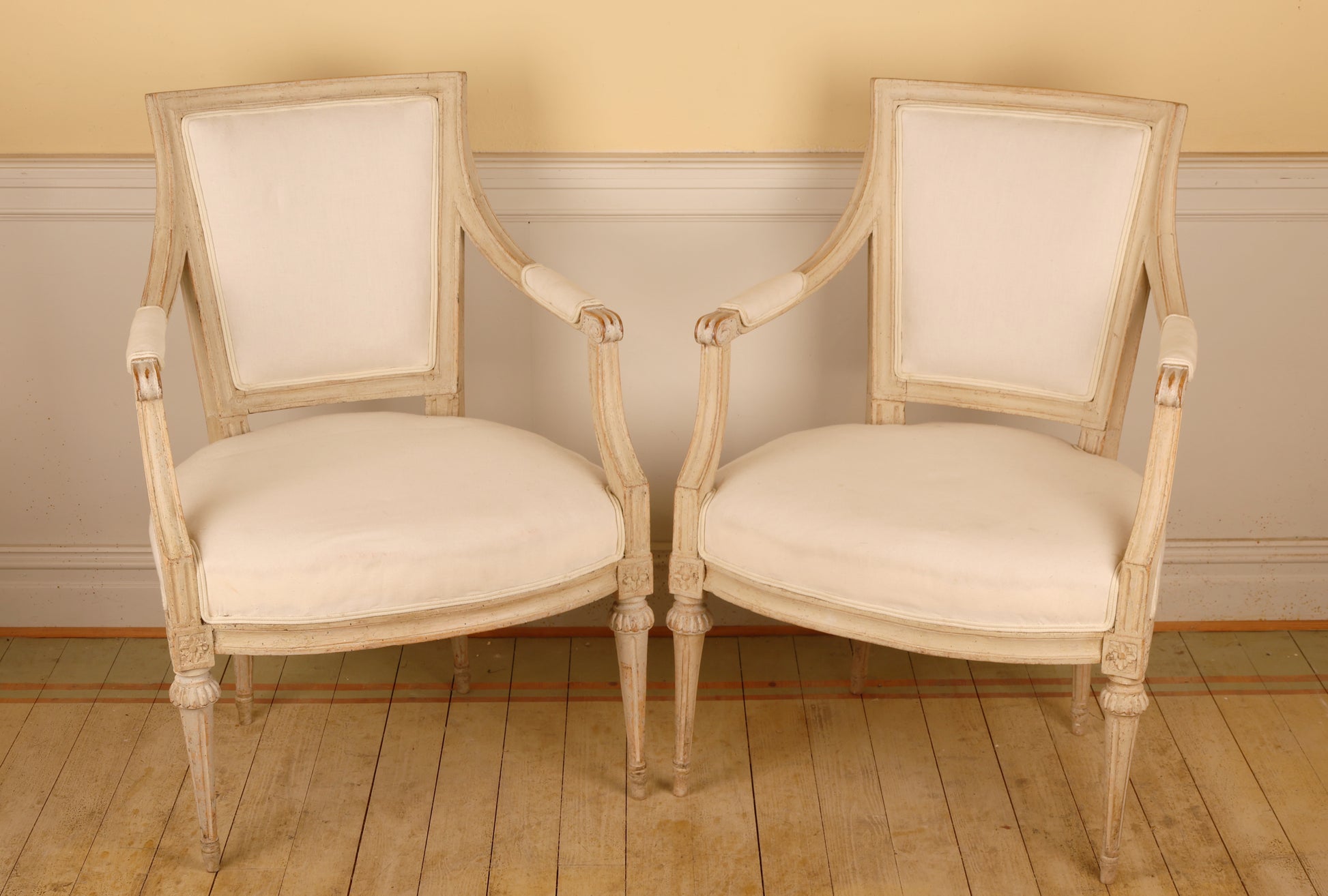 A pair of pearl-grey Gustavian armchairs from the late 18th century with white upholstery. The chairs feature carved leaf motifs and stand on collared, fluted legs.