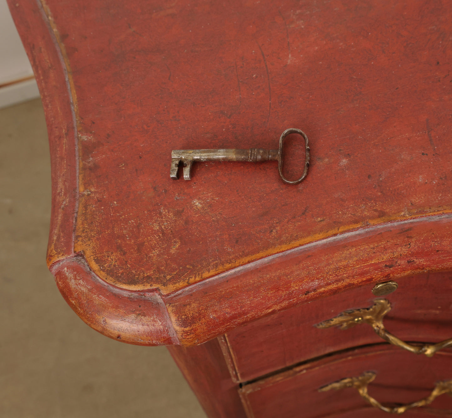 The key to unlock an 18th Century Baroque Chest of Drawers in a lovely red color with gilded details.