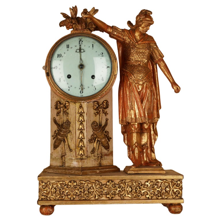 An 19th century Empire mantel clock in gilded wood, with a warrior in classical armor such as helmet, chestpiece with scales and a cape. The clock pillar is adorned with ribbons and bows and arrows.