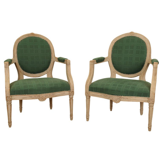 Pair of Gustavian armchairs with carved flower decorations and green upholstery.