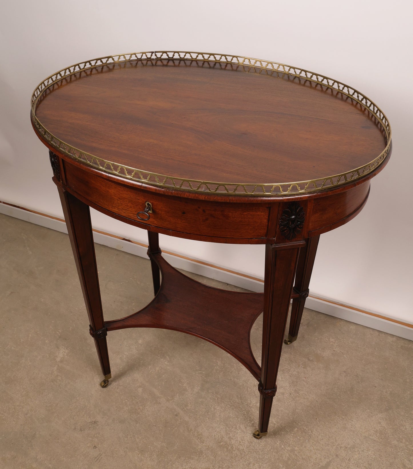 High-class Stockholm piece from around 1790. Crafted in veneered and partially solid mahogany with carved wooden decorations of corner florets. The core material is pine and alder. The top is fitted with a brass balustrade. The table features brass castors and includes a drawer in the apron with a key.