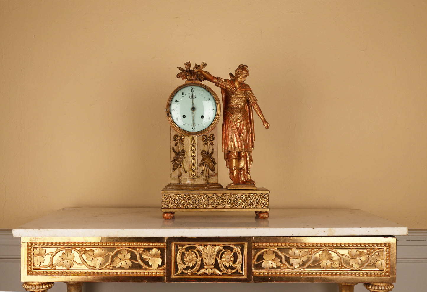 An 19th century Empire mantel clock in gilded wood, with a warrior in classical armor such as helmet, chestpiece with scales and a cape. The clock pillar is adorned with ribbons and bows and arrows.