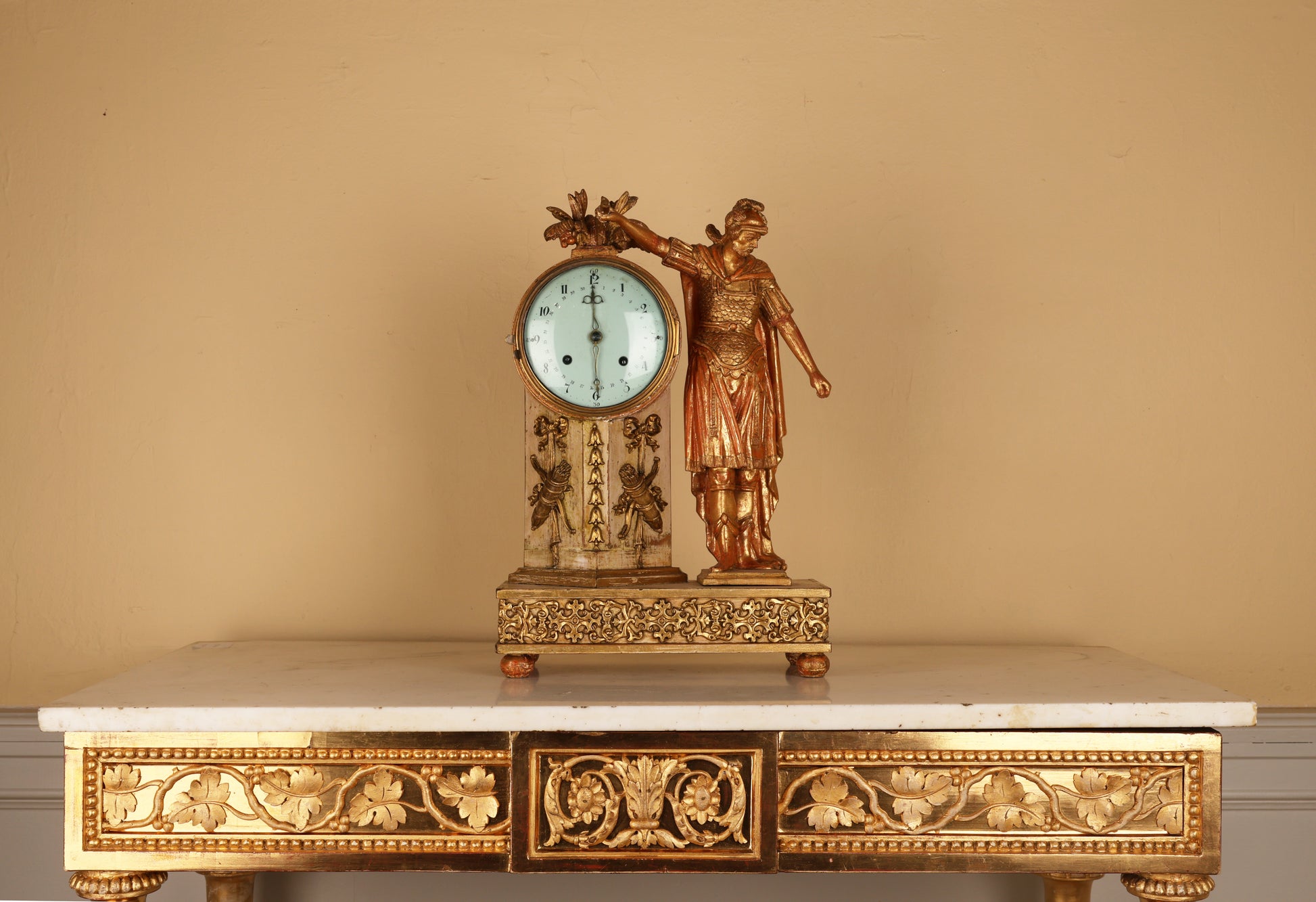 An 19th century Empire mantel clock in gilded wood, with a warrior in classical armor such as helmet, chestpiece with scales and a cape. The clock pillar is adorned with ribbons and bows and arrows.