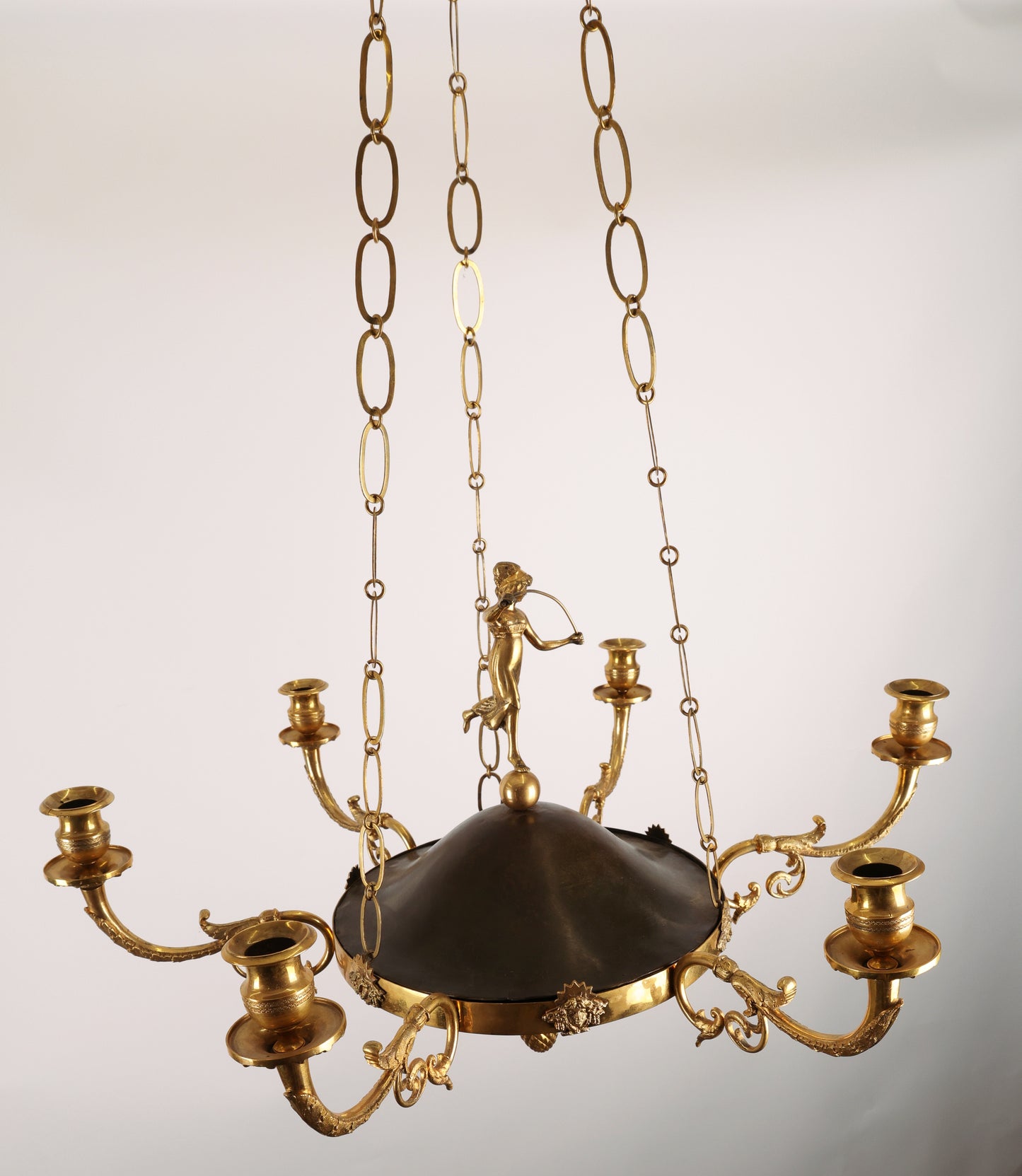 High-class Empire pendant from Stockholm around 1800-1810. It features six beautifully decorated candle arms with acanthus leaves. The central decoration includes a female figure standing on a sphere. Three chains support the pendant, which culminates at the top with a plate before the ceiling hook. The ring is adorned with Medusa heads. The pendant is finished at the bottom with a decoration of a pine cone in fire-gilded bronze.