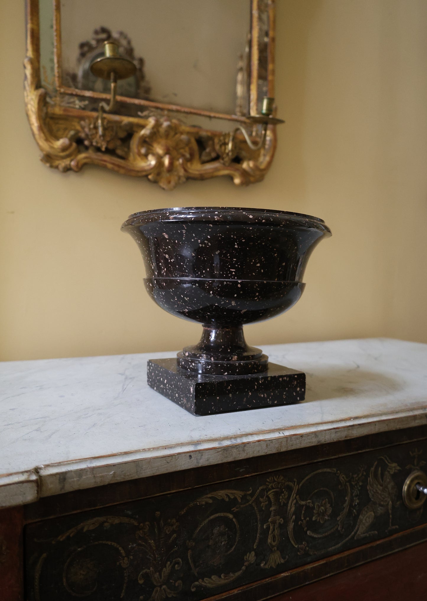 Porphyry Urn standing on a chest of drawers with a gilded mirror in the background