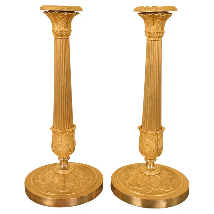 A pair of French burnished gilded Empire candlesticks with light collars. The stems are fluted and decorated with acanthus leaves. With white background.