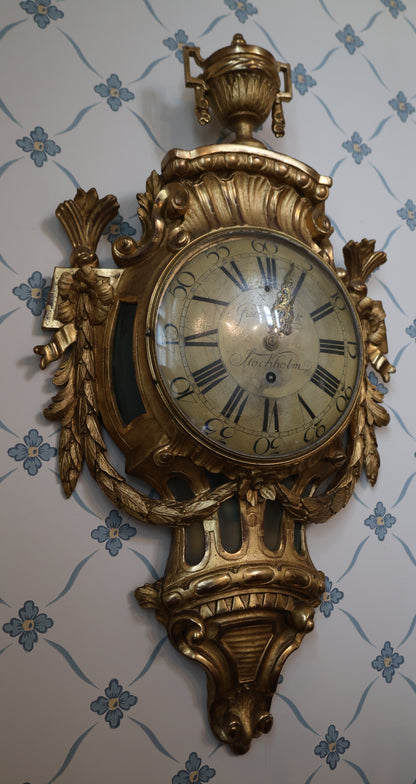 Wall Clock signed Jacob Kock from the transitional period between Rococo and Gustavian styles. The case is entirely carved from wood and gilded.