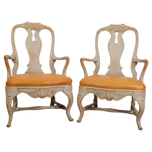 A pair of high-quality Rococo armchairs, made in Stockholm (Sweden) in the 1760s. The chairs feature elegant carvings in the form of rocailles on the top rail and the apron. The colour is a restored original finish. The seats are upholstered in leather. White background.