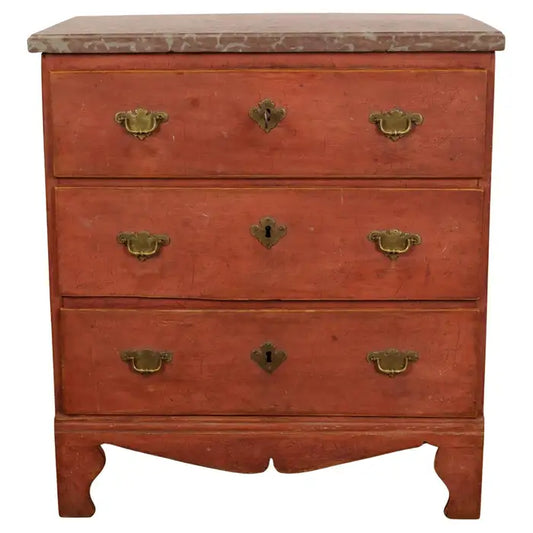 A small red chest of drawers from the Baroque period. The chest was provincially made in Southern Sweden. The limestone top is from Öland. The hardware is cast bronze. The chest has three drawers. White background.