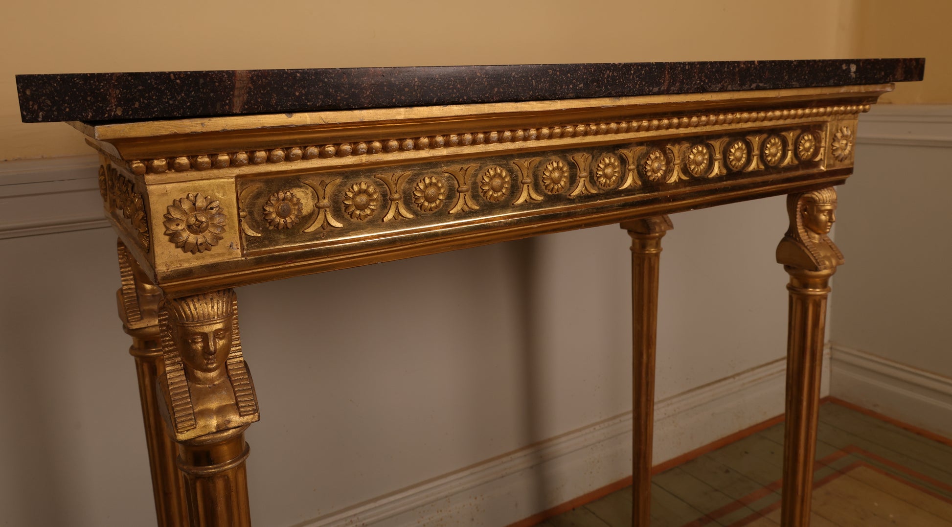 Close up of a golden high-quality Gustavian console table made in Stockholm in the 19th century. The legs feature carved Egyptian-inspired heads and fluted details. The top is porphyry.