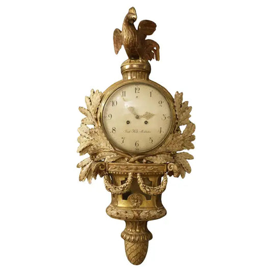 Large Gustavian wall clock with a movement signed by Jacob Kock (1737-1805). This pendulum features a spectacular design, crowned with a rooster at the top. The enameled movement is surrounded by floral swags. The glass in front of the movement is original. The lower part has double garlands and is finished with a large pinecone. The case has its original gilding. With white background.