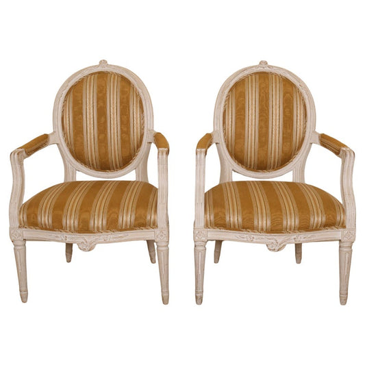 A pair of exceptional Gustavian armchairs crafted in Stockholm during the 1780s. These chairs represent the classic medallion-back style that was widely popular during the period. They are of the larger model, offering both generous proportions and excellent comfort. The legs are elegantly adorned with gadrooned fluting, adding sophistication to the design. The front rail and the top of the backrest feature finely carved floral details, while the leg joints to the rail are enhanced with graceful florets.