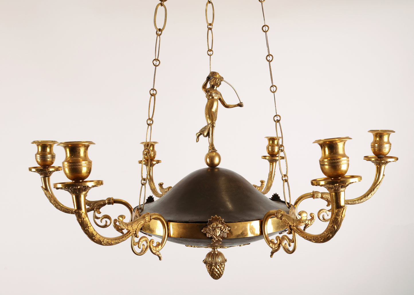 High-class Empire pendant from Stockholm around 1800-1810. It features six beautifully decorated candle arms with acanthus leaves. The central decoration includes a female figure standing on a sphere. Three chains support the pendant, which culminates at the top with a plate before the ceiling hook. The ring is adorned with Medusa heads. The pendant is finished at the bottom with a decoration of a pine cone in fire-gilded bronze.