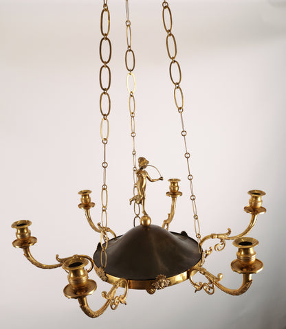 High-class Empire pendant from Stockholm around 1800-1810. It features six beautifully decorated candle arms with acanthus leaves. The central decoration includes a female figure standing on a sphere. Three chains support the pendant, which culminates at the top with a plate before the ceiling hook. The ring is adorned with Medusa heads. The pendant is finished at the bottom with a decoration of a pine cone in fire-gilded bronze.