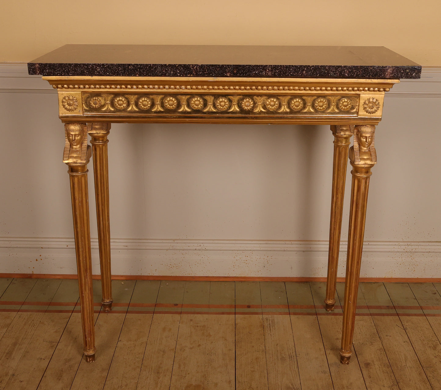 A high-class late Gustavian gilt console table made in Stockholm around 1800. The legs feature carved Egyptian-inspired heads and fluted details. The table's frieze is decorated with a carved bead border and floral motifs. The top is an original slab of porphyry.